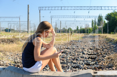 Teenager girl with mobile sitting on unfinished rail track