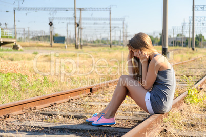 Upset teenager girl sitting on rail track in countryside