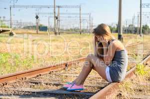 Upset teenager girl sitting on rail track in countryside