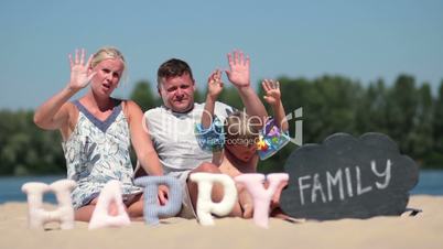 Happy family sitting on the beach and waving hello