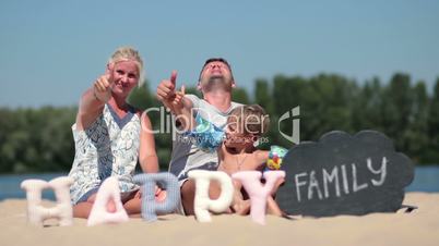 Family sitting on the beach and giving thumbs up