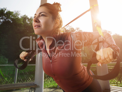 Young beautiful woman doing fitness training with suspension straps.