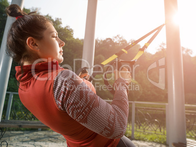 Young beautiful woman doing fitness training with suspension straps.