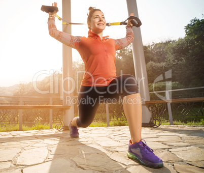 Young beautiful woman doing fitness training with suspension straps.