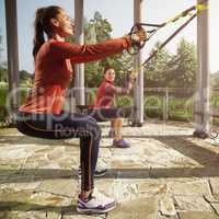 Young beautiful woman doing fitness training with suspension straps.