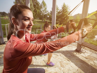 Young beautiful woman doing fitness training with suspension straps.