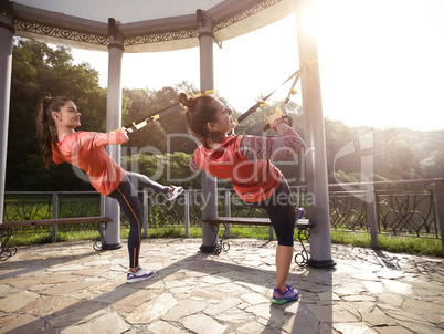 Young beautiful woman doing fitness training with suspension straps.