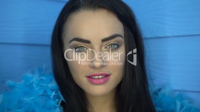 Closeup of beautiful brunette woman smiling and looking into the camera with blue feather boa over blue wall background