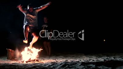 People jumping over bonfire on the beach at night