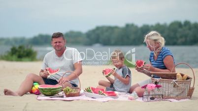 Happy family eating watermelon on the beach