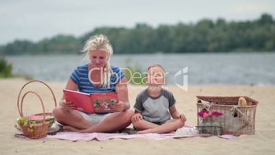 Mother reading book to cute son at the beach