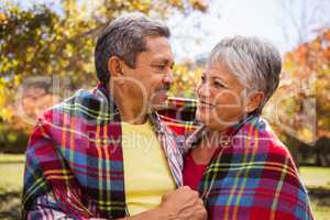 Elderly couple sitting on bench smiling at each other with a bl