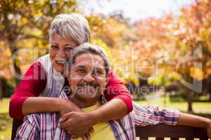 An elderly woman hugs her husband sitting on the bench looking a