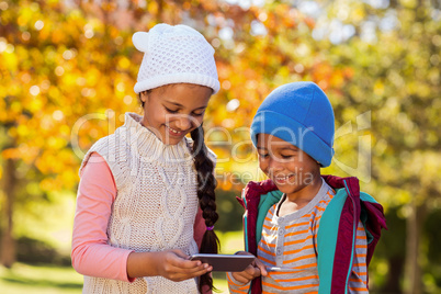 Happy siblings using mobile phone at park