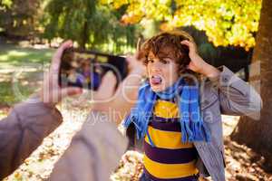 Cropped image of girl photographing boy making face in park