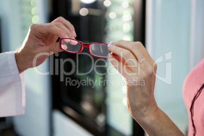 Optometrist giving spectacles to customer in optical store