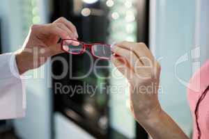 Optometrist giving spectacles to customer in optical store