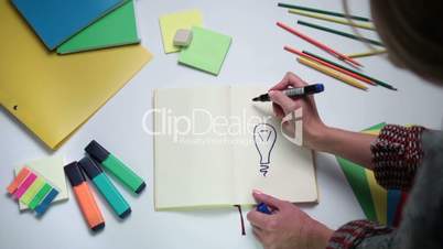 Girl writing word idea on notepad above lightbulb