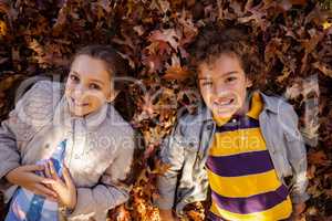 High angle portrait of smiling siblings lying on autumn leaves