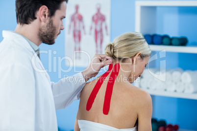 Physiotherapist sticking tape on female patient