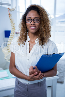 Smiling physiotherapist holding clipboard in clinic