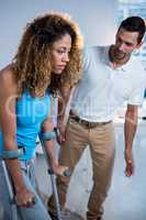Physiotherapist helping his patient walking with crutch