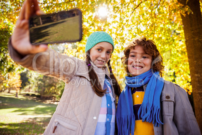 Smiling siblings taking selfie at park during autumn