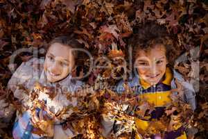 Portrait of happy siblings lying on autumn leaves at park