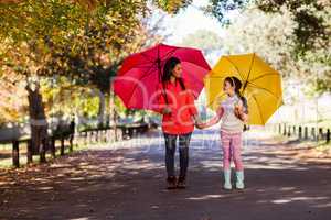 Mother and daughter holding umbrellas at park