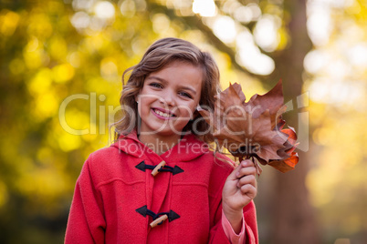 Smiling girl holding autumn leaves at park