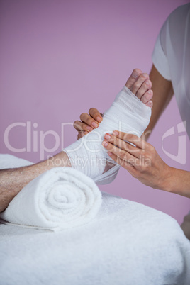 Physiotherapist putting bandage on injured feet of patient