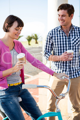 Couple with coffee cups having fun with a bicycle