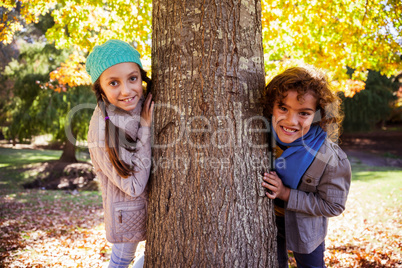 Portrait of smiling siblings leaning on tree trunk at park