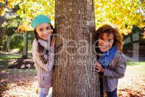 Portrait of smiling siblings leaning on tree trunk at park