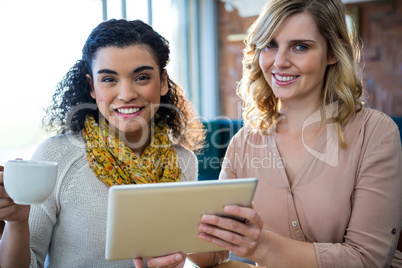 Female friends using digital tablet while having coffee