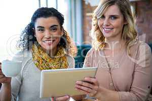 Female friends using digital tablet while having coffee