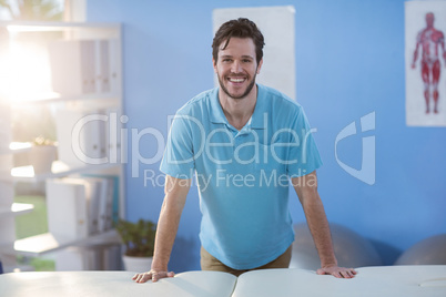 Portrait of male physiotherapist standing near massage bed