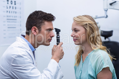 Optometrist examining female patient through ophthalmoscope