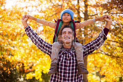 Father carrying son on shoulder against autumn trees
