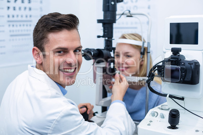 Smiling optometrist examining female patient on slit lamp