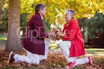 Mature couple holding autumn leaves while kneeling