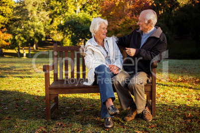 Elderly couple sitting on bench smiling at each other in park