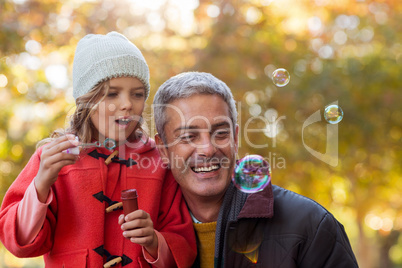 Smiling father with daughter blowing bubbles at park