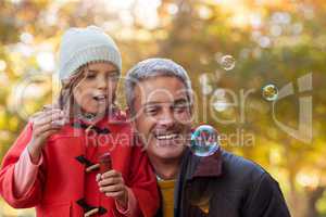 Smiling father with daughter blowing bubbles at park