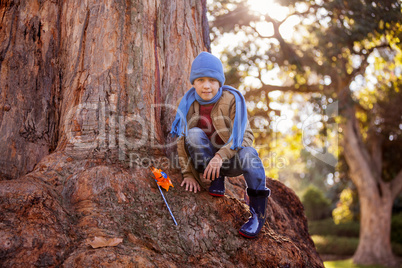 Portrait of boy with pinwheel while crouching on tree trunk