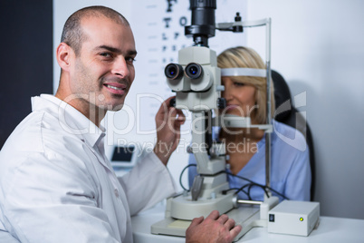 Smiling optometrist examining female patient on slit lamp