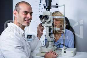 Smiling optometrist examining female patient on slit lamp