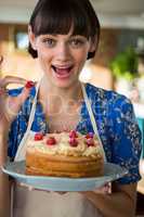 Excited waitress holding a cake and showing a cherry