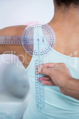 Physiotherapist measuring female patients back with medical rule