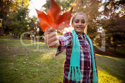 Portrait of smiling girl showing autumn leaf at park